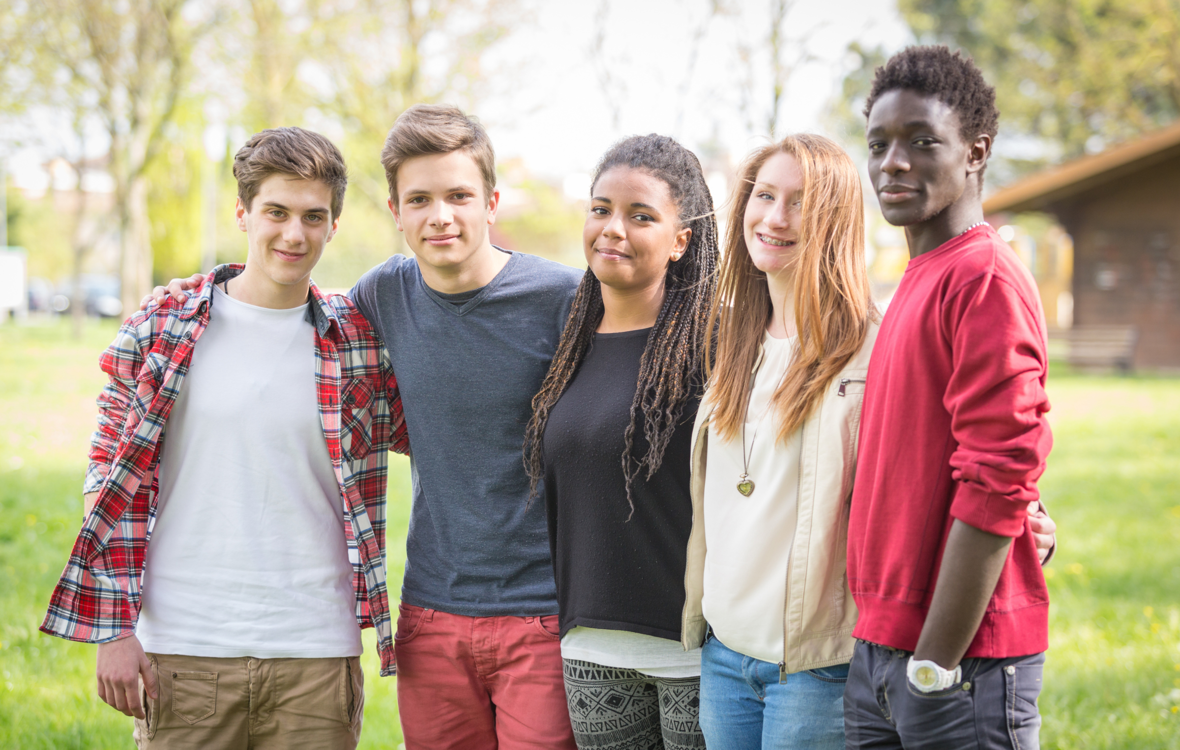 Group of teens smiling looking at the camera with their arms around each other.