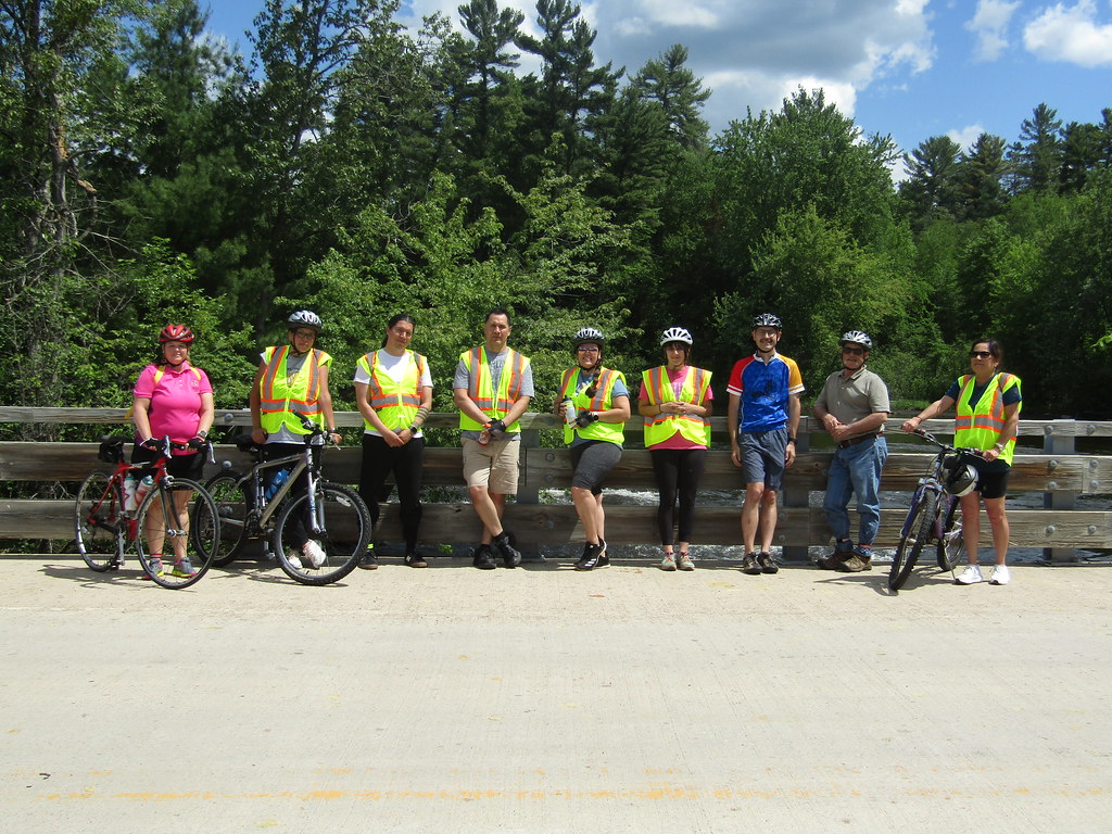 Individuals standing a on bridge with bikes, helmets, and reflective vests.
