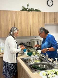 Two women standing at a sink canning cucumbers.