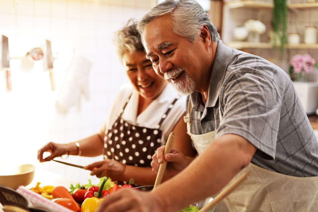 Two older adults in the kitchen cooking with peppers on a tray